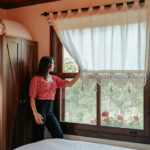 Woman enjoying sunlight in a cozy budget guesthouse room, a perfect example of cheap stays in USA for travelers.